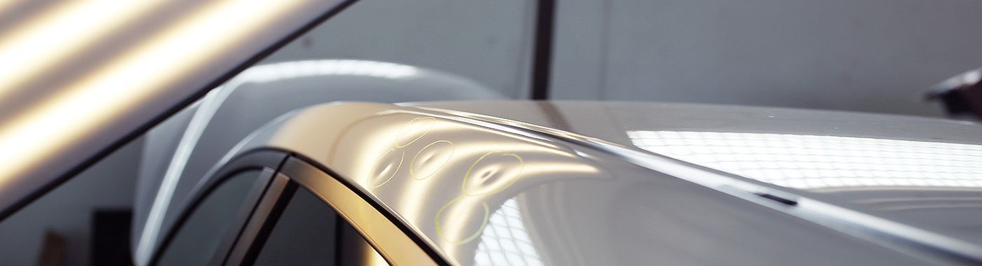Car roof with multiple dents, being inspected under bright lights.