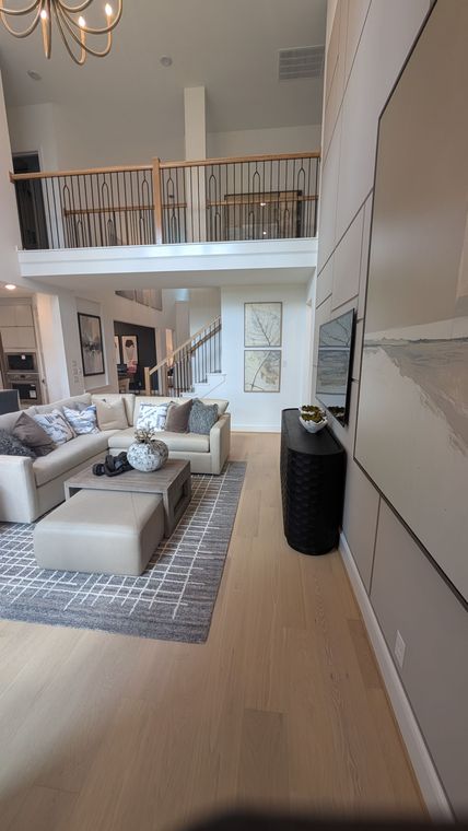 Bright living room with beige sectional, patterned rug, balcony railing, and tall white storage cabinets