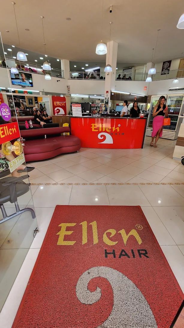 Entrada da loja Ellen Hair com um capacho vermelho de boas-vindas. O interior possui balcão vermelho de recepção e clientes.