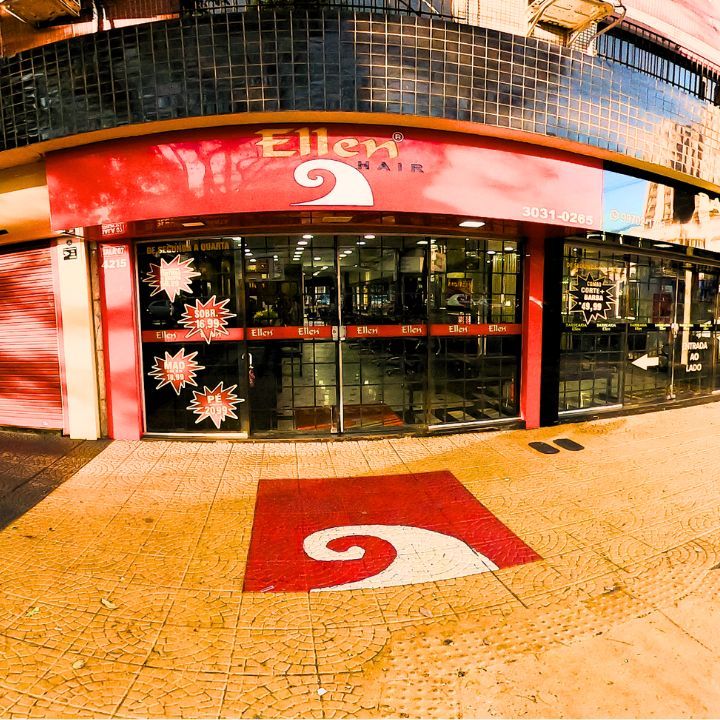 Exterior do salão Ellen Hair com sinalização vermelha e branca no chão e portas de vidro.