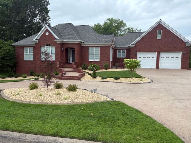 Red brick house with white garage doors, tan driveway, and landscaped yard.