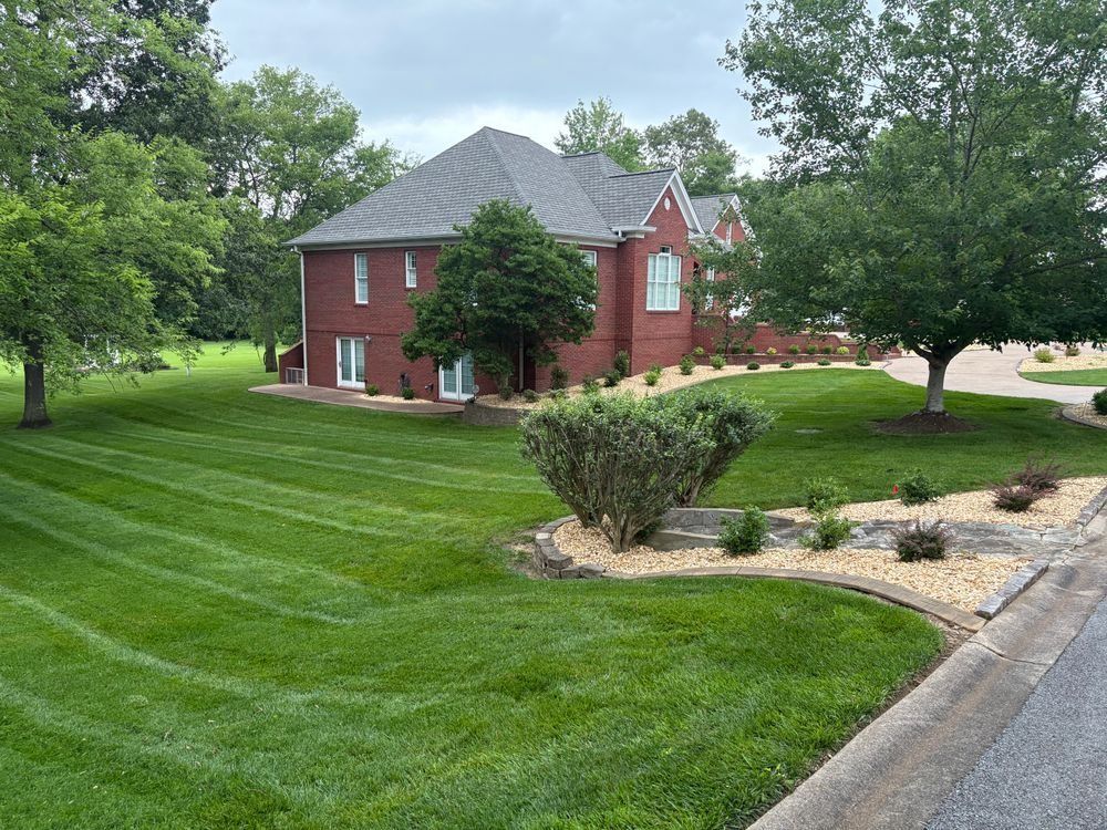 Red brick house with well-manicured green lawn and landscaping. Overcast day.