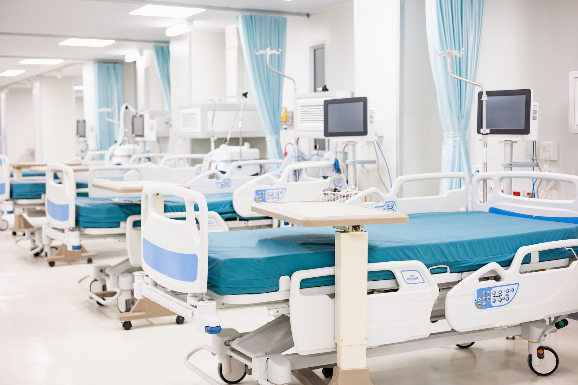 A row of hospital beds in an empty hospital room.