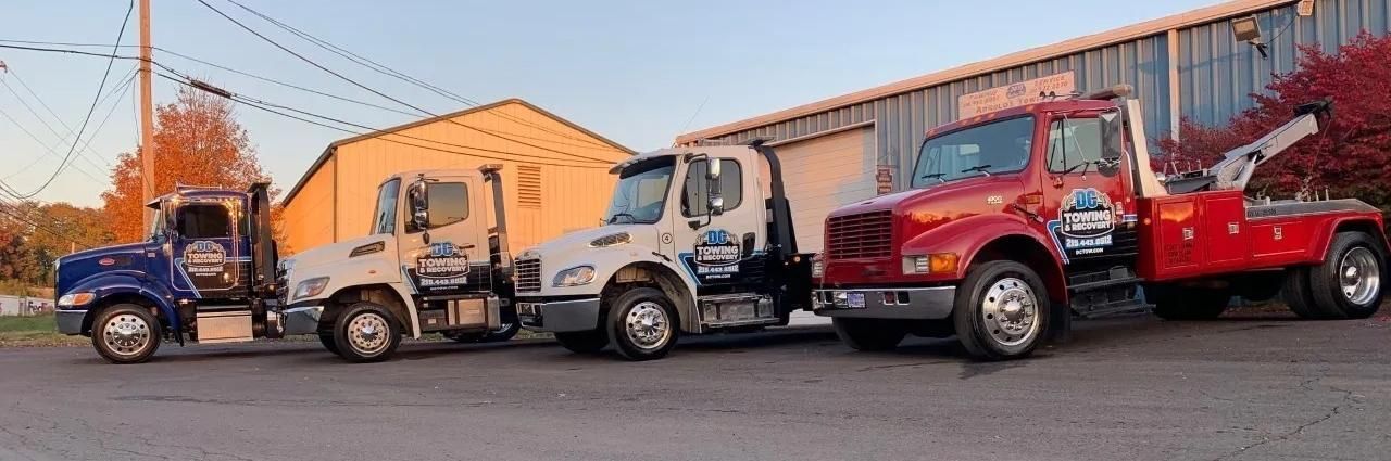 Tow trucks in blue, white, and red lined up outside a garage at dusk