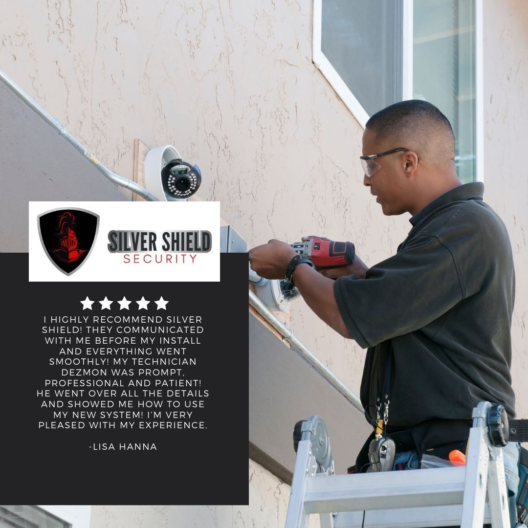 Security technician installing a surveillance camera beside a Silver Shield Security sign.