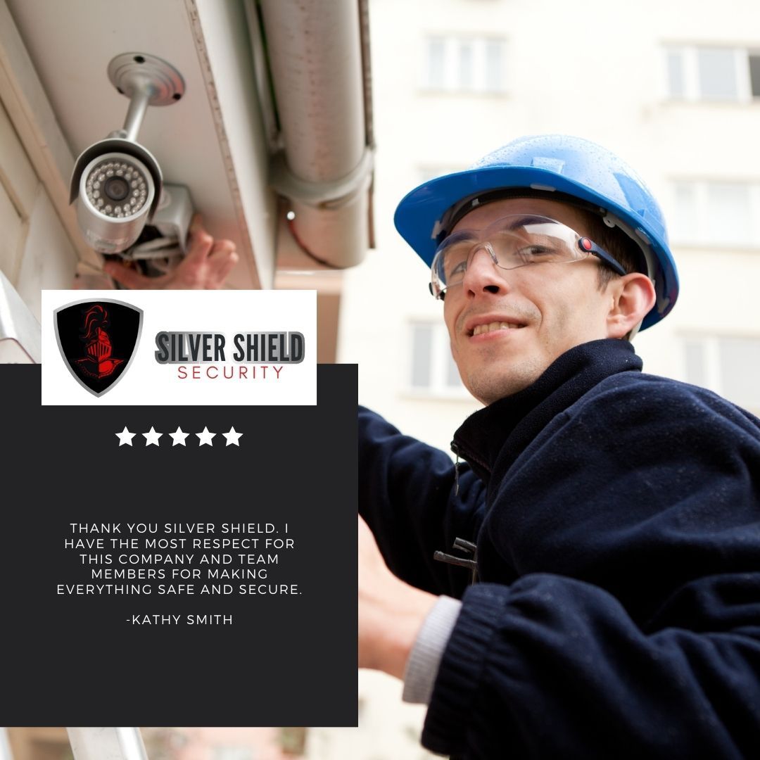 Security technician in blue hard hat beside a ceiling camera and Silver Shield Security ad