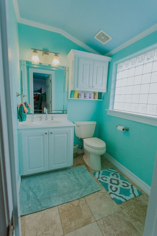 A bathroom with blue walls , a toilet , a sink , and a window.