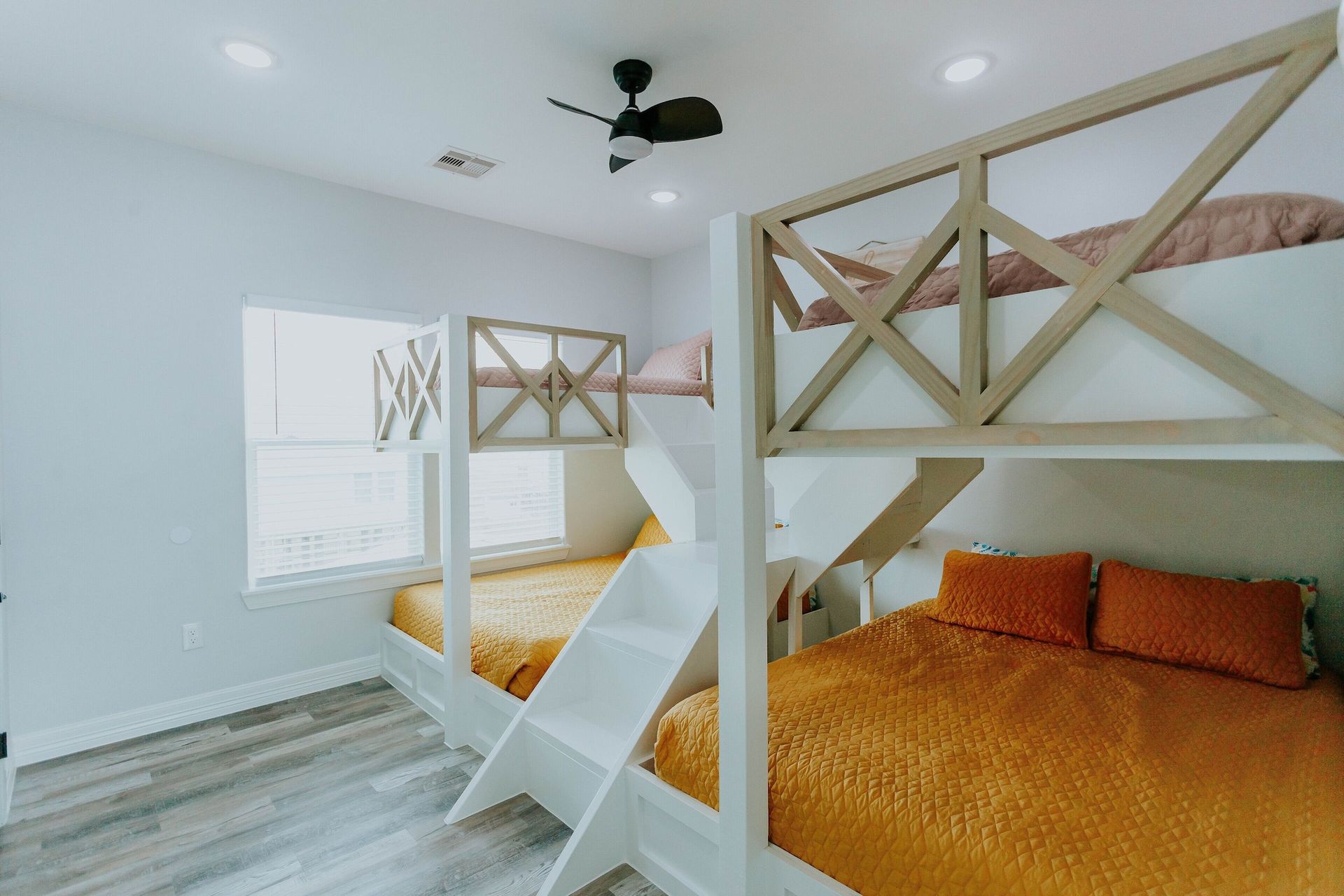 A room featuring a large, white L-shaped bunk bed with mustard yellow bedding and a staircase leading to the top bunks.