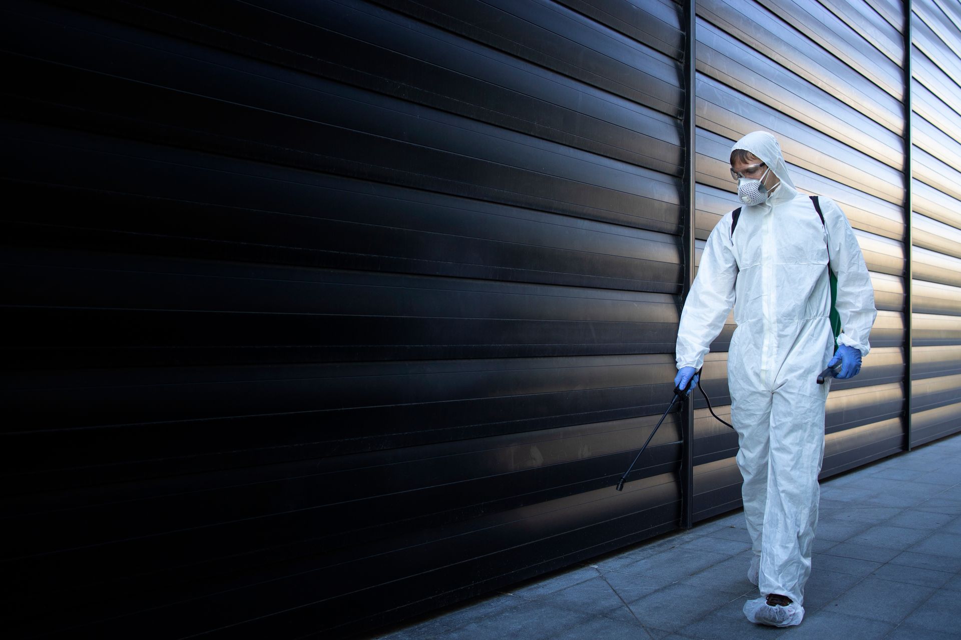 Person spraying insulation into an attic. Pest control technician in a white suit spraying building exterior.