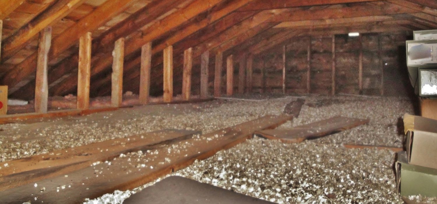 An attic space filled with insulation. Wooden beams and support columns are visible throughout.