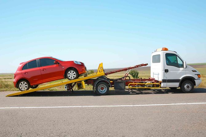 Red car loaded on a tow truck along a roadside under a clear blue sky