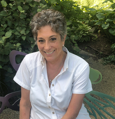A woman in a white shirt is sitting on a green chair and smiling.