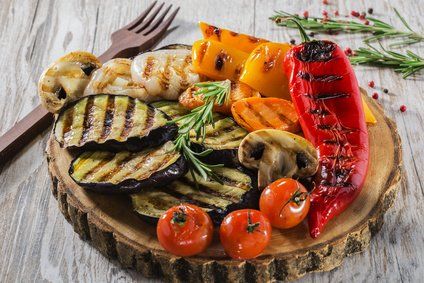 A wooden cutting board topped with grilled vegetables and a fork.