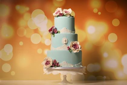 A blue wedding cake with flowers on top is on a cake stand.