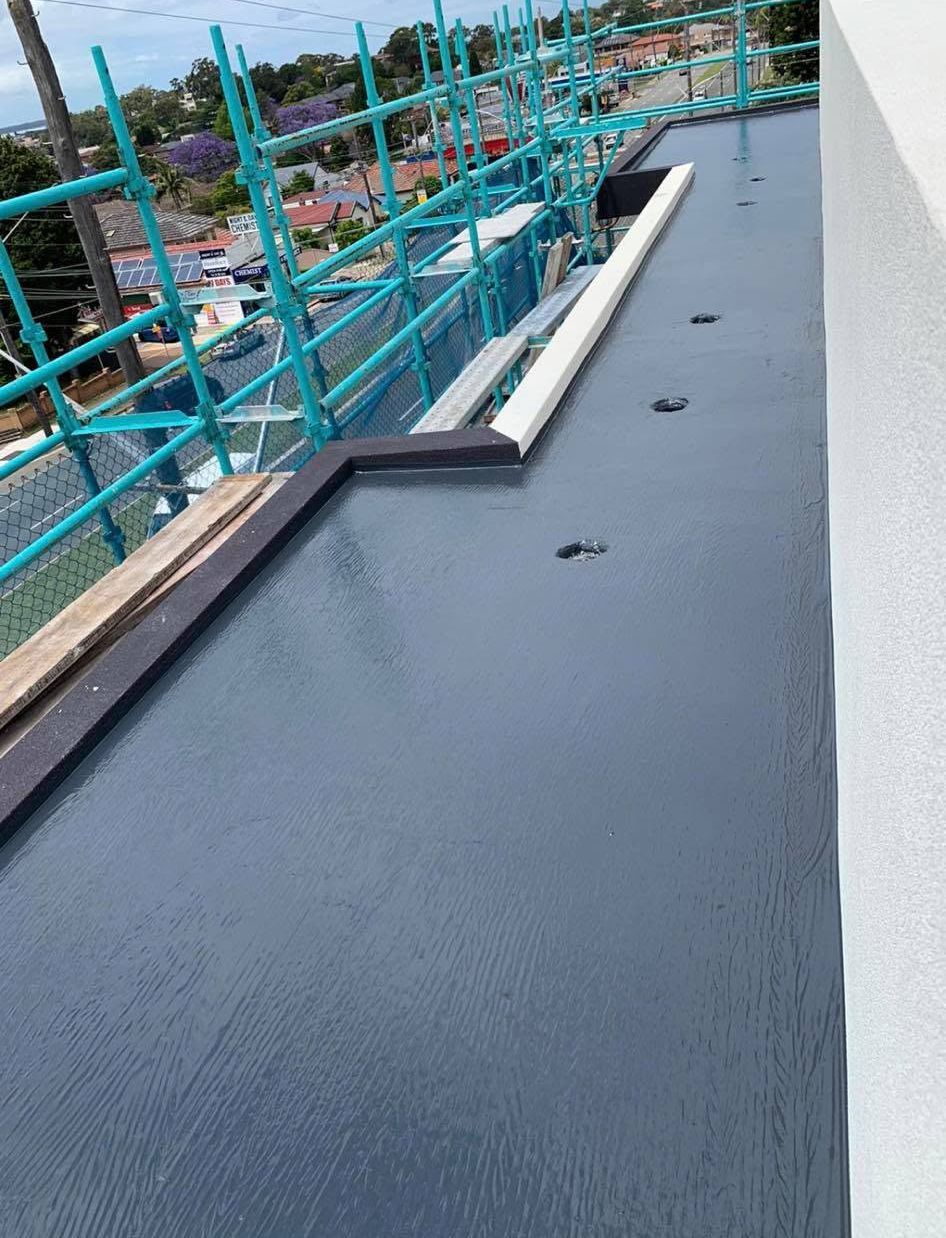 Flat rooftop walkway with dark waterproof coating and turquoise safety railings