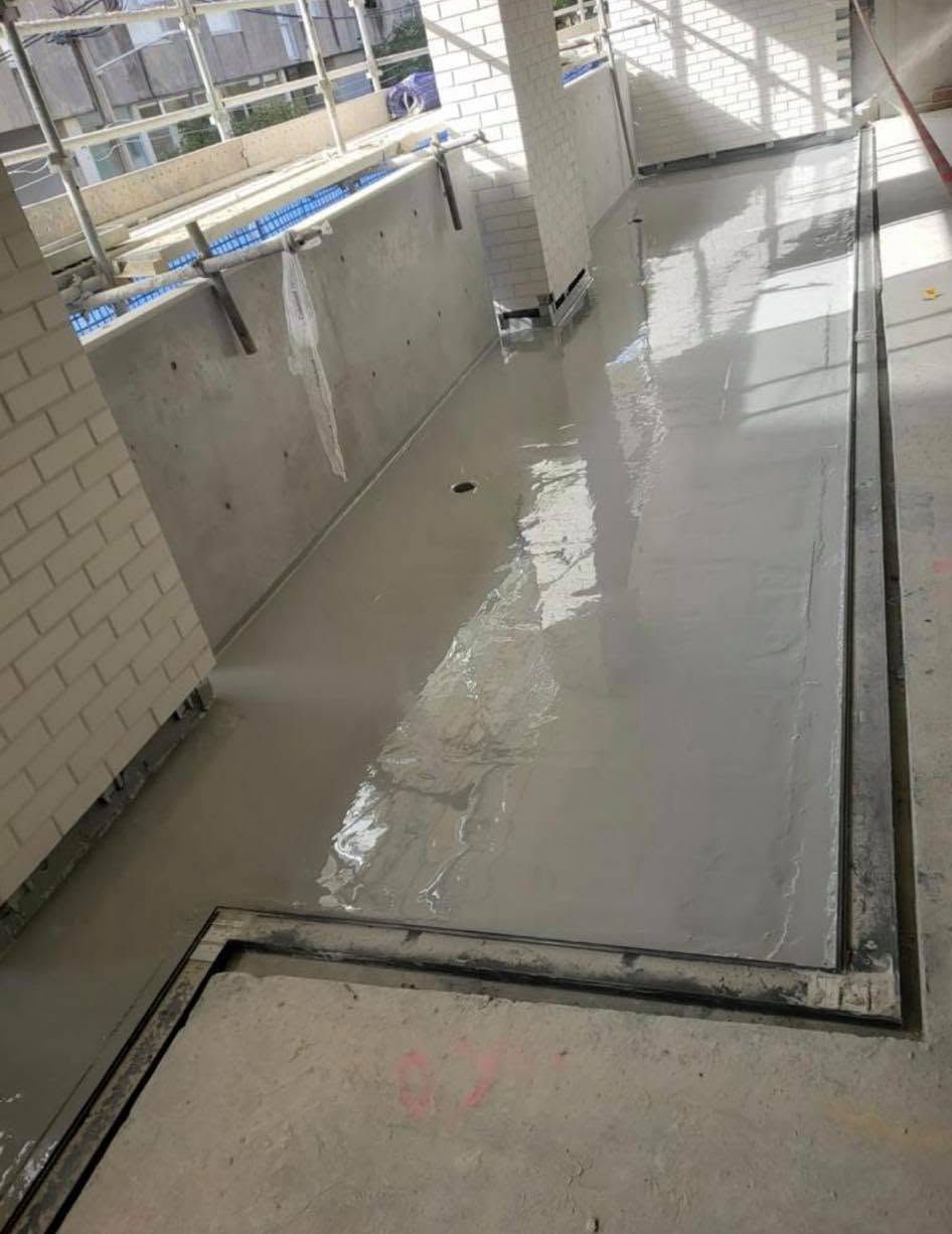 Indoor concrete corridor under construction with wet floor and white tiled walls, viewed from above