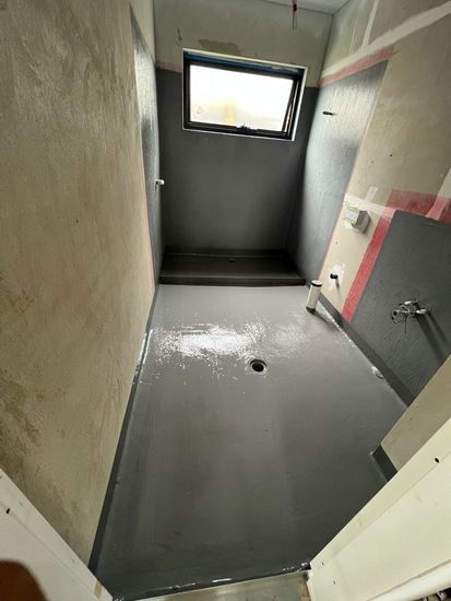 Empty concrete swimming pool being coated with light blue waterproof paint, with a pipe in the foreground.