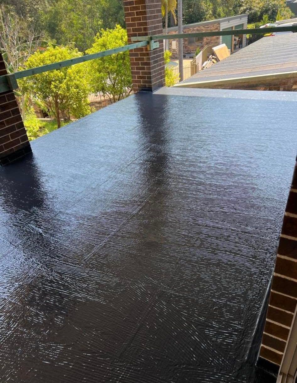 Black textured patio tabletop on a porch with brick columns and a railing overlooking greenery
