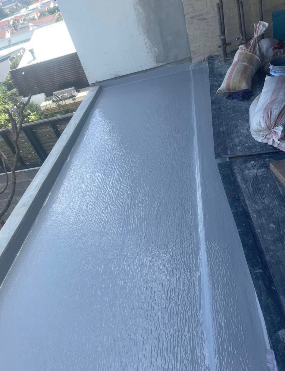 Gray waterproofed rooftop with a sloped surface and construction materials along the edge