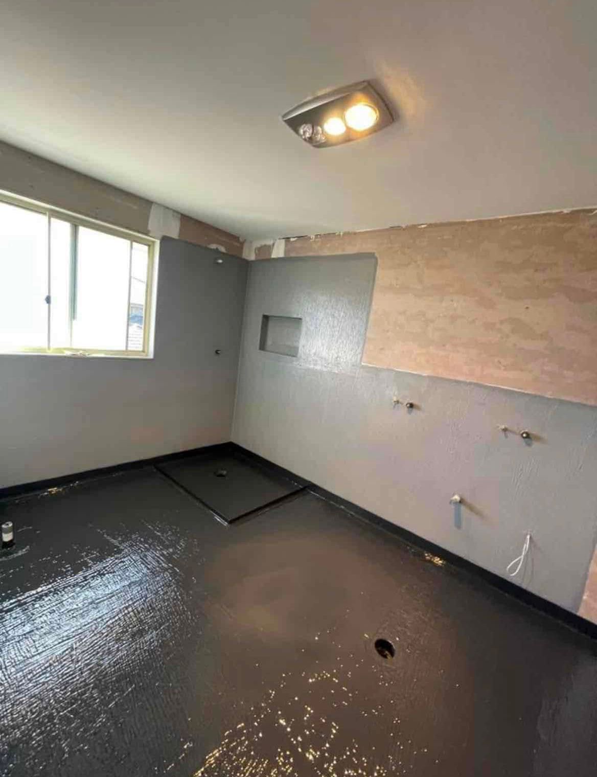 Empty room with wet black floor, gray walls, window, and ceiling light during renovation