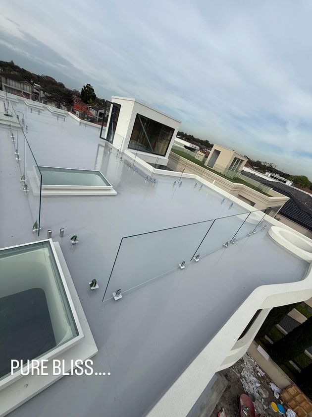 Rooftop terrace with a curved white surface, glass railings, and distant buildings under an overcast sky.