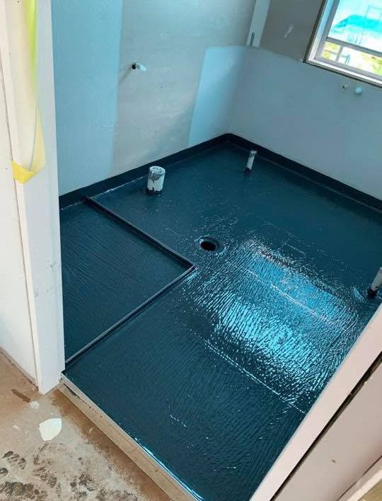 Small bathroom under renovation with dark waterproof floor coating and a drain hole.