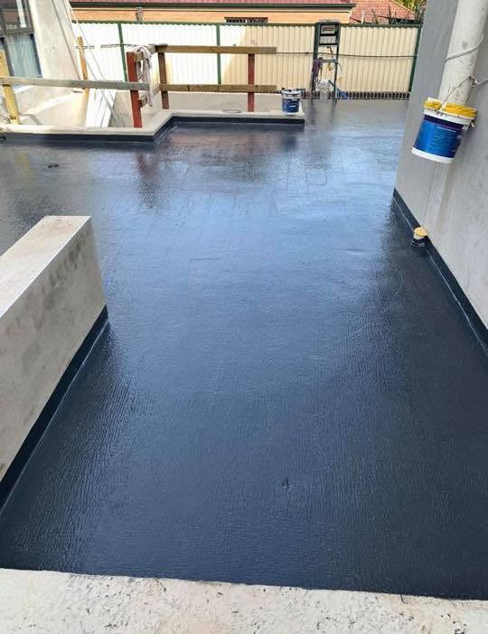 Freshly coated dark blue rooftop terrace with low walls and a bucket near the railing.