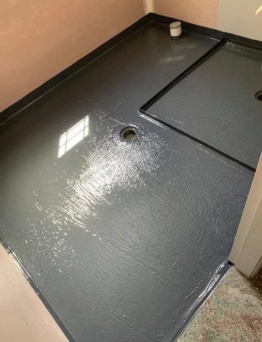 Gray waterproofed shower floor with a drain and a small access panel in the corner