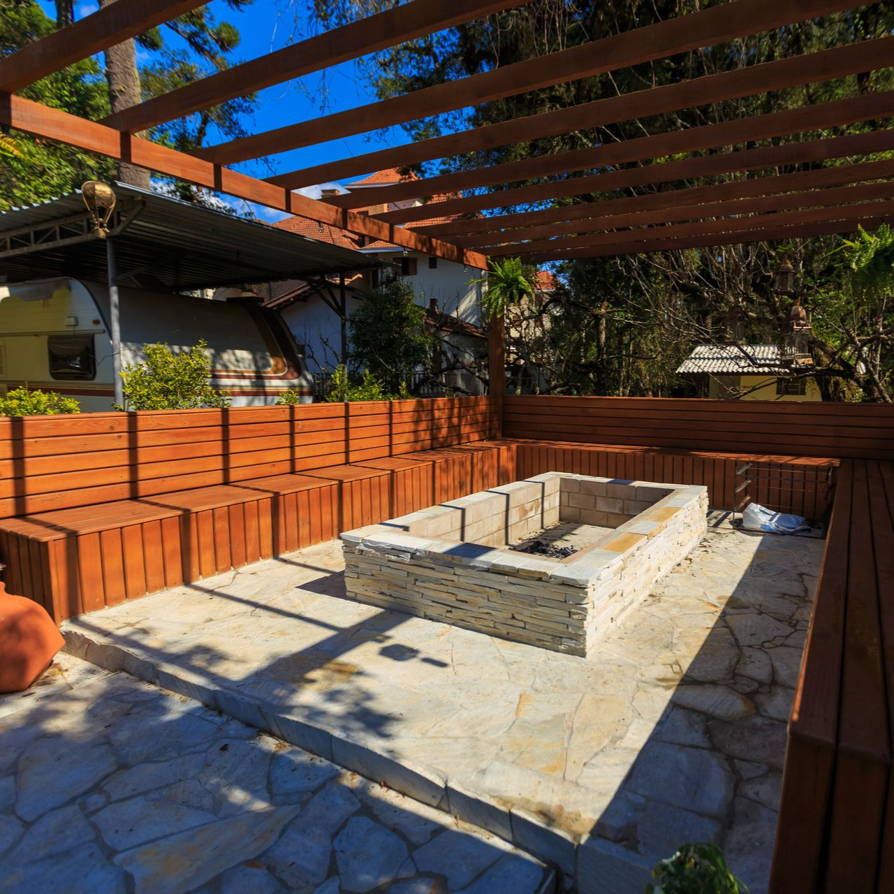 Stone fire pit in a backyard patio with red brick seating walls and a wooden pergola overhead