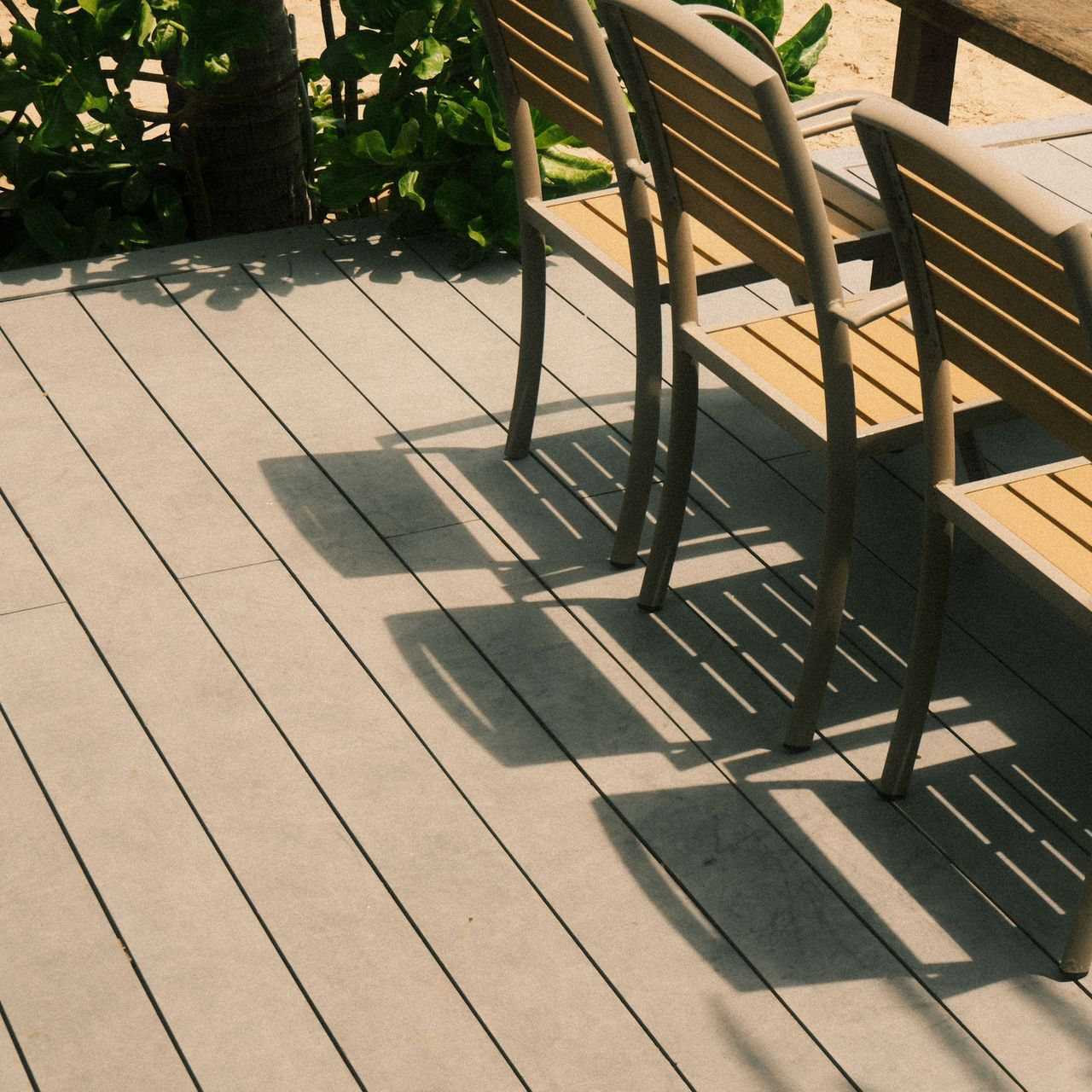 Wooden deck with two chairs casting long shadows in warm sunlight