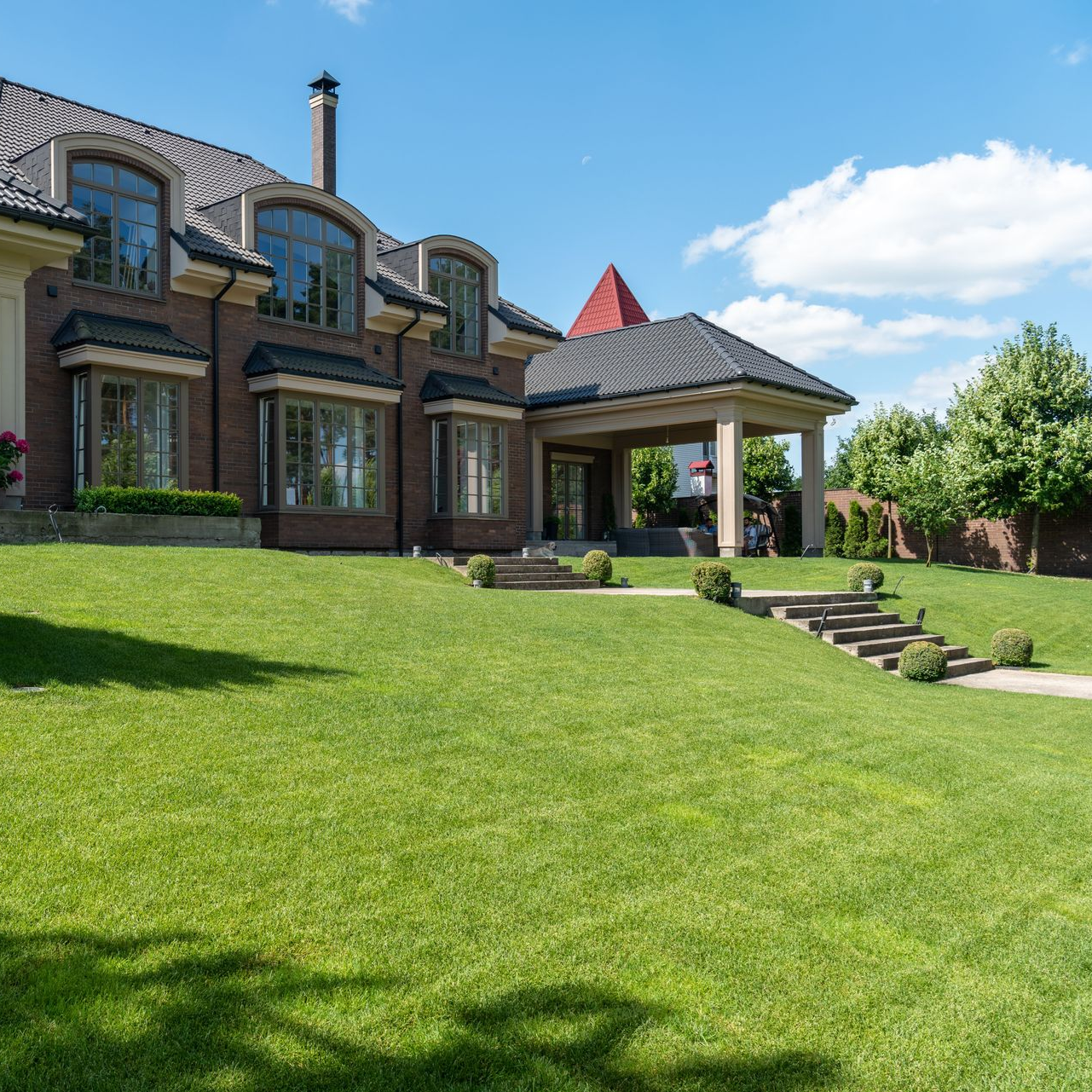 Brick house with a green lawn, stone steps, and a covered porch under a blue sky