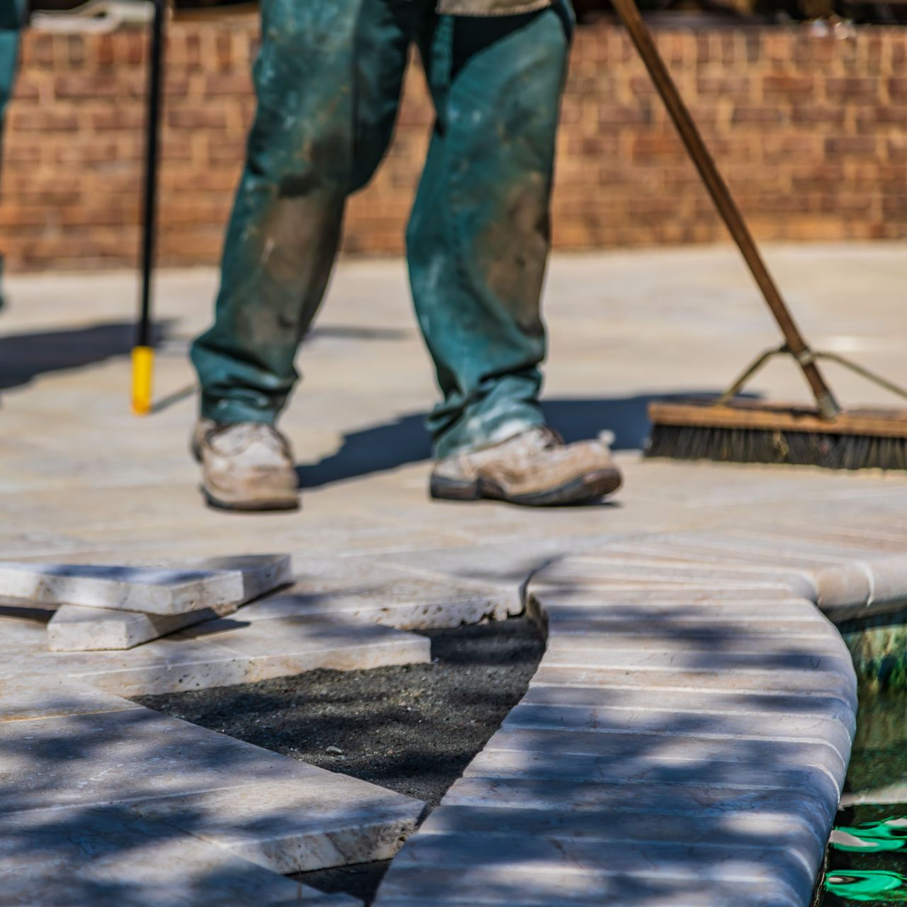 Worker sweeping dust off a concrete surface near bricks and pavers on a rooftop or patio