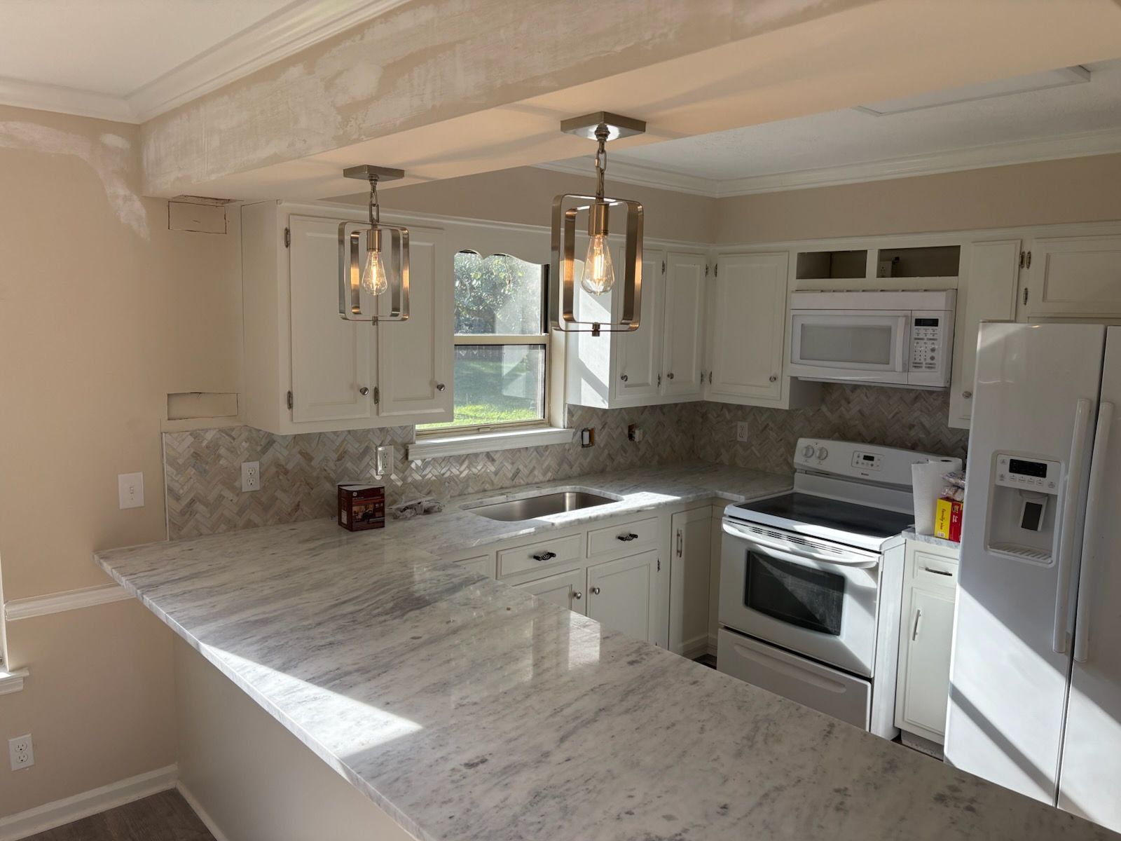 White kitchen with a granite countertop, cabinets, and stainless steel pendant lights.