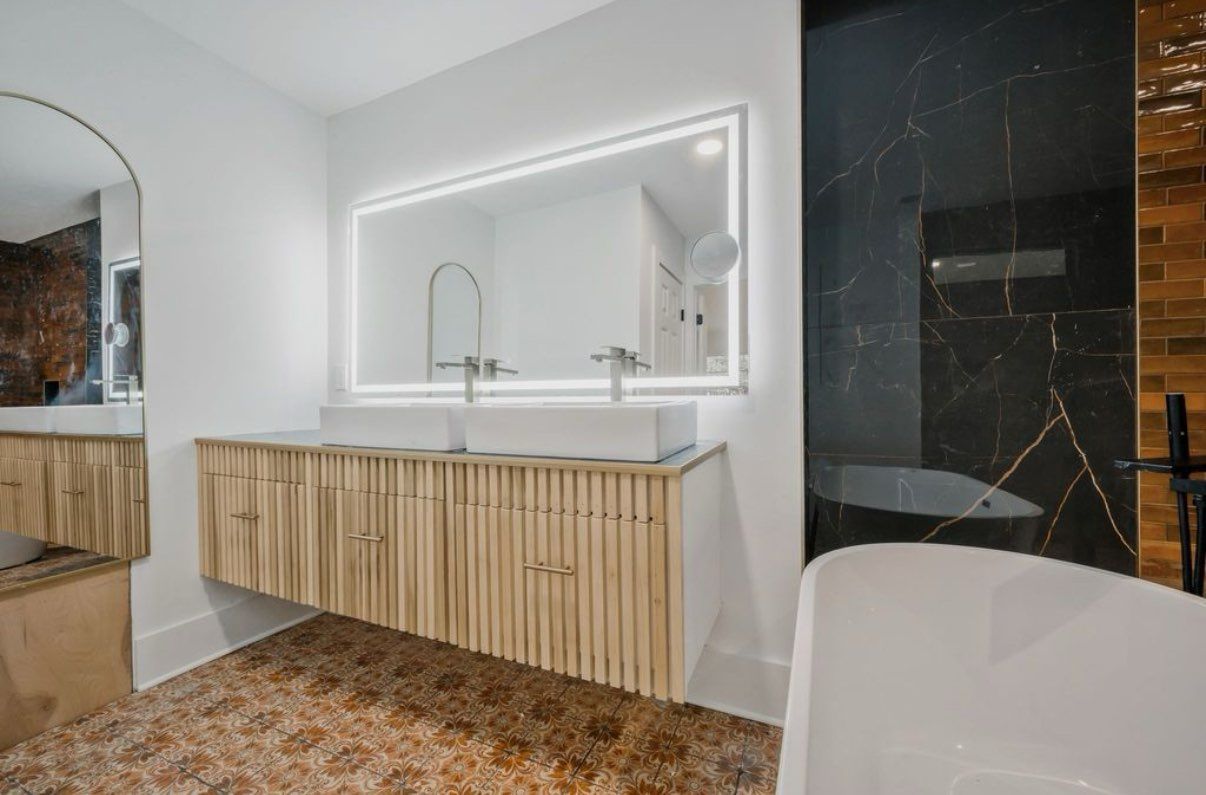 Modern bathroom with floating vanity, large mirror, bathtub, and textured wall.