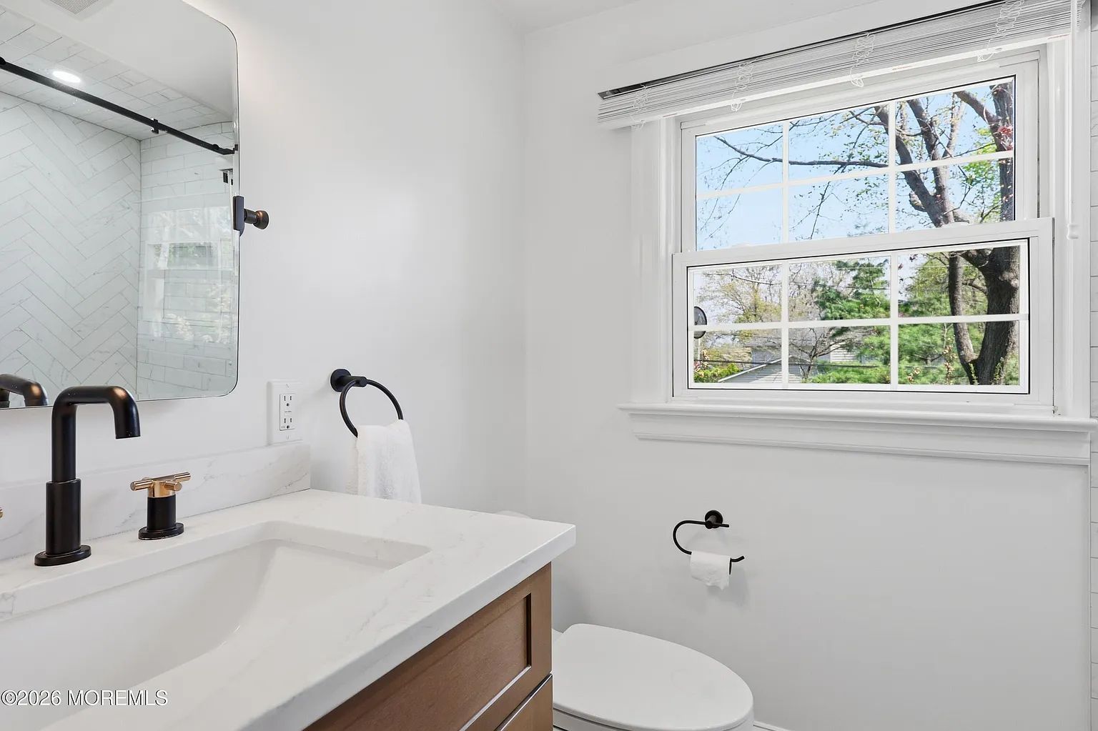 Bright white bathroom with black fixtures, vanity sink, toilet, and window letting in natural light