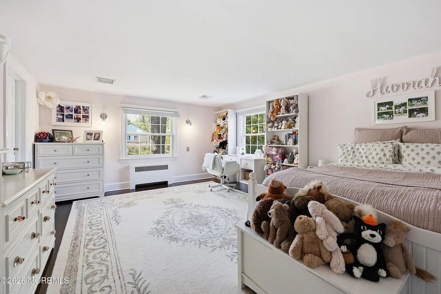 Bright white child's bedroom with twin beds, plush toys, pink accents, and shelves of dolls and books.