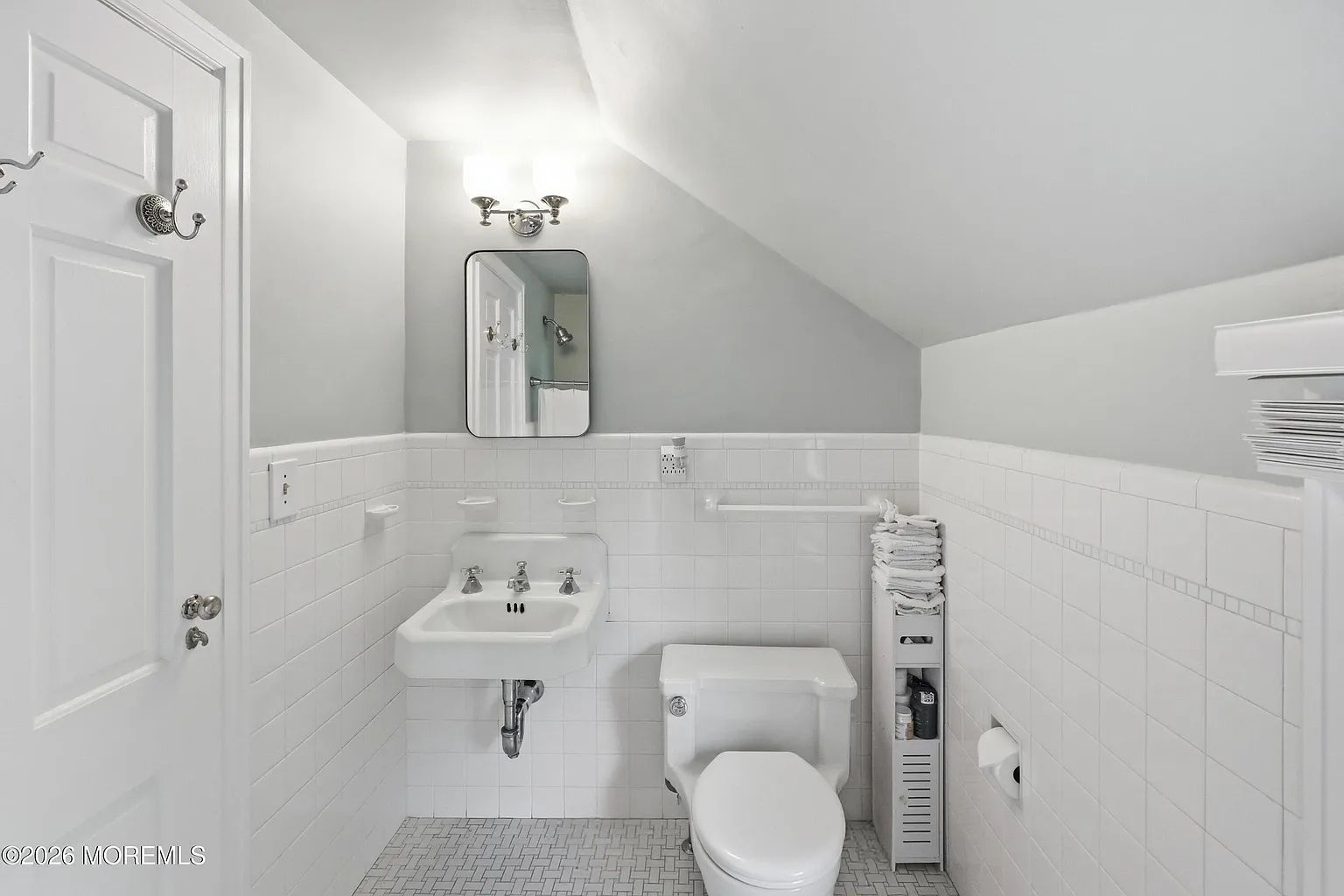 Bright white bathroom with sink, toilet, wall mirror, and towel rack under a sloped ceiling