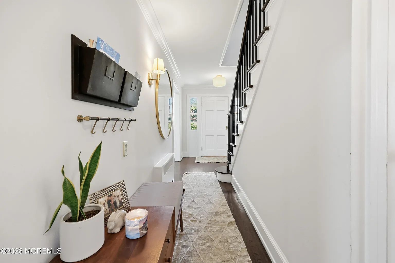 Narrow hallway with white walls, wooden console table, wall-mounted TV, stairway, and runner rug