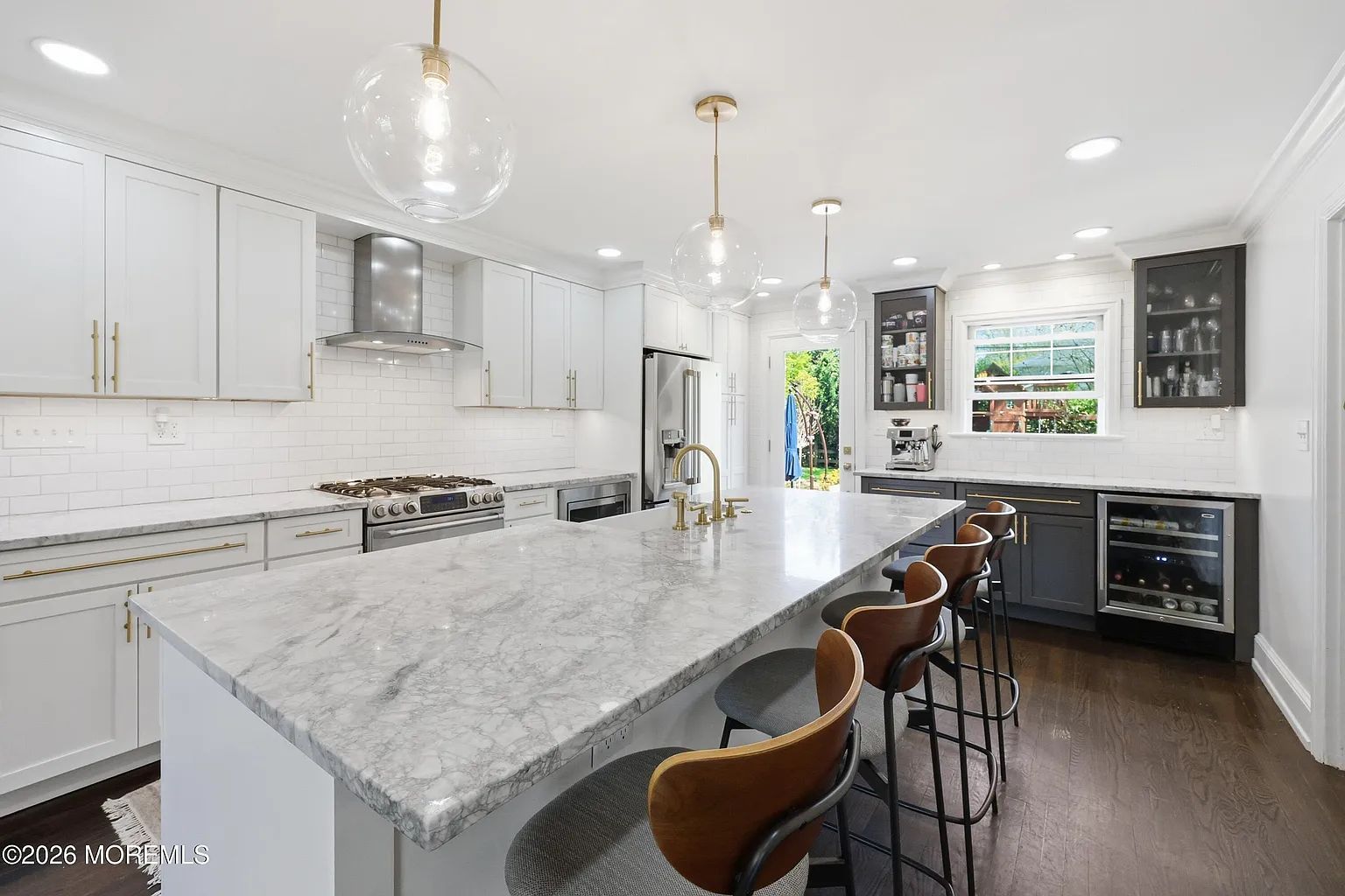 Bright white modern kitchen with large marble island, barstools, pendant lights, and stainless steel appliances