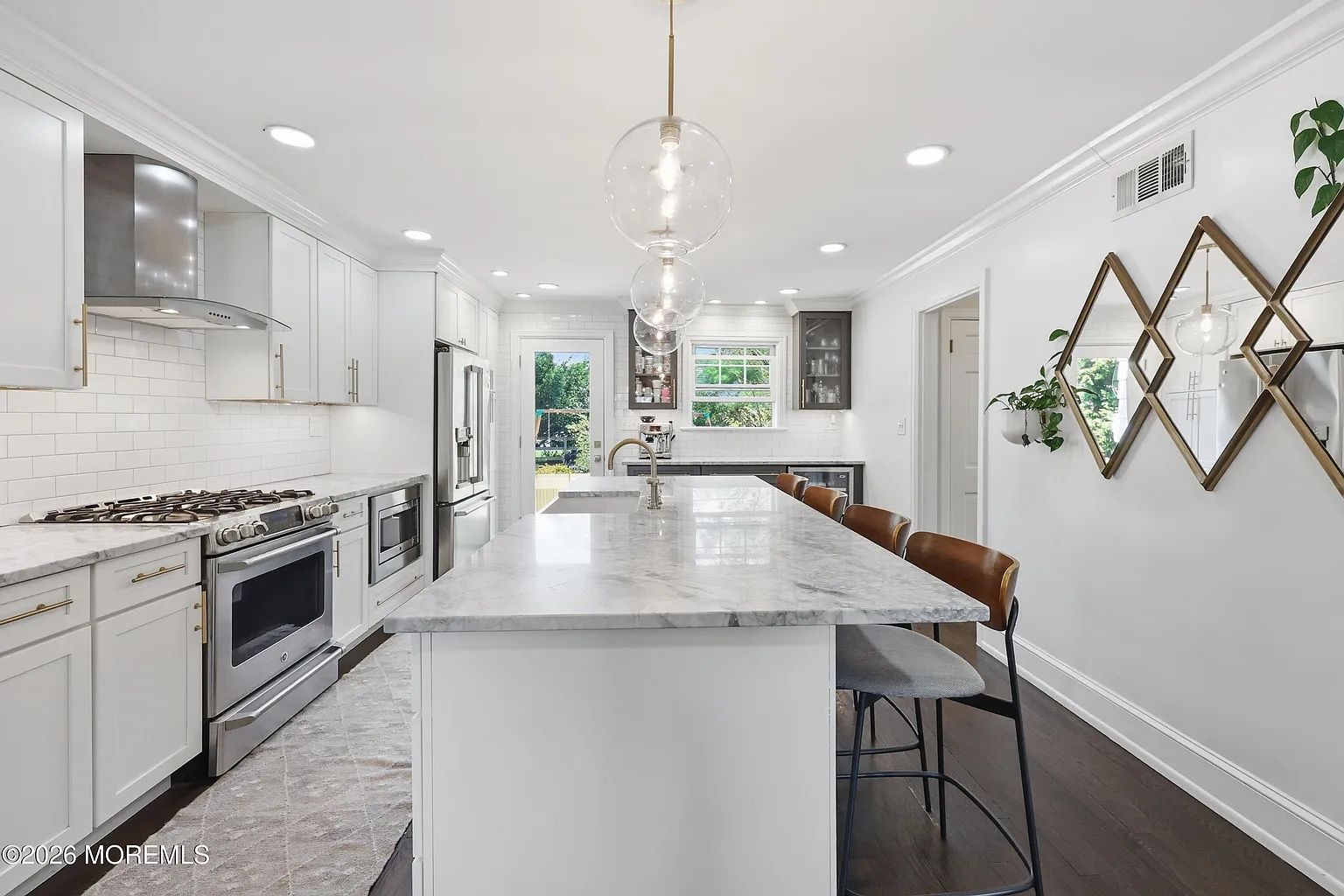 Bright white galley kitchen with marble island, stainless appliances, and wall decor shelves