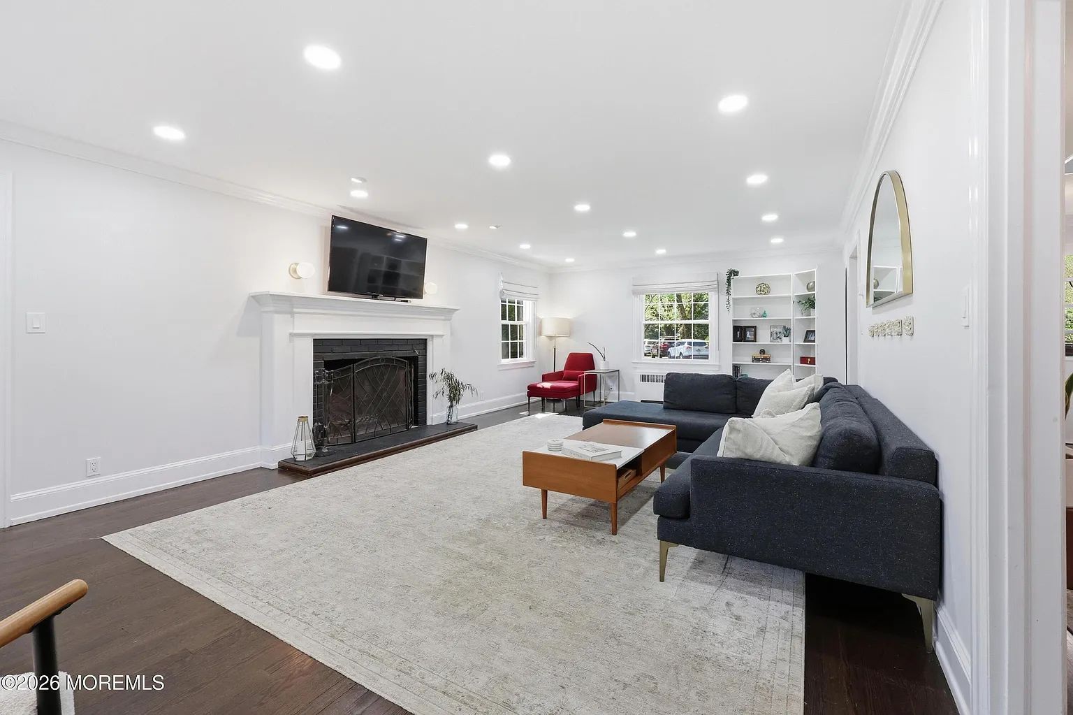 Bright white living room with fireplace, gray sofa, wood coffee table, and TV mounted above the mantel.