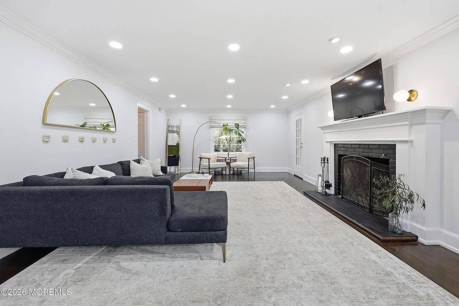 Bright modern living room with dark sofa, white fireplace, large rug, and recessed lighting