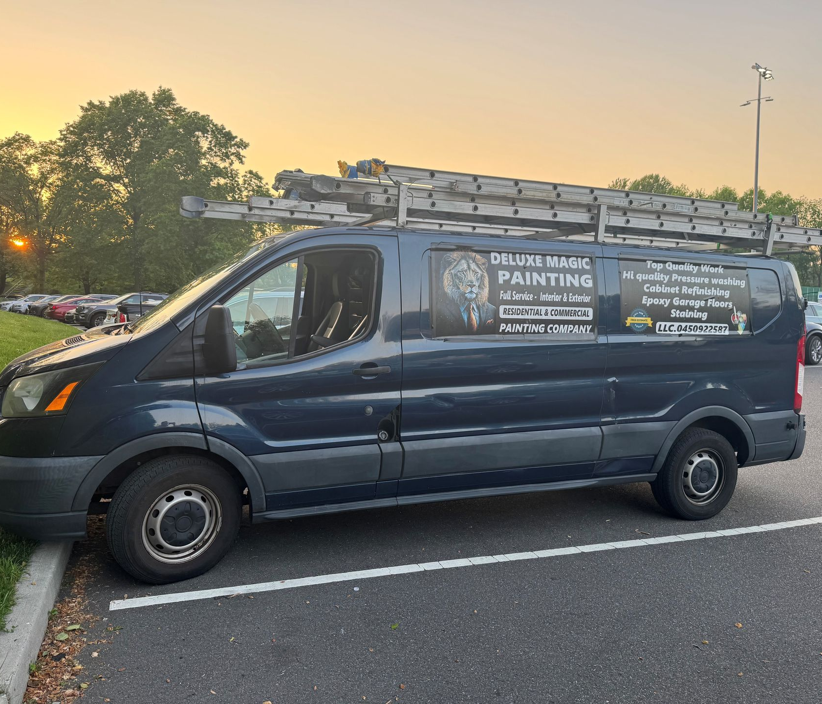 Blue service van with ladder racks and a phone number parked at sunset, labeled for painting services
