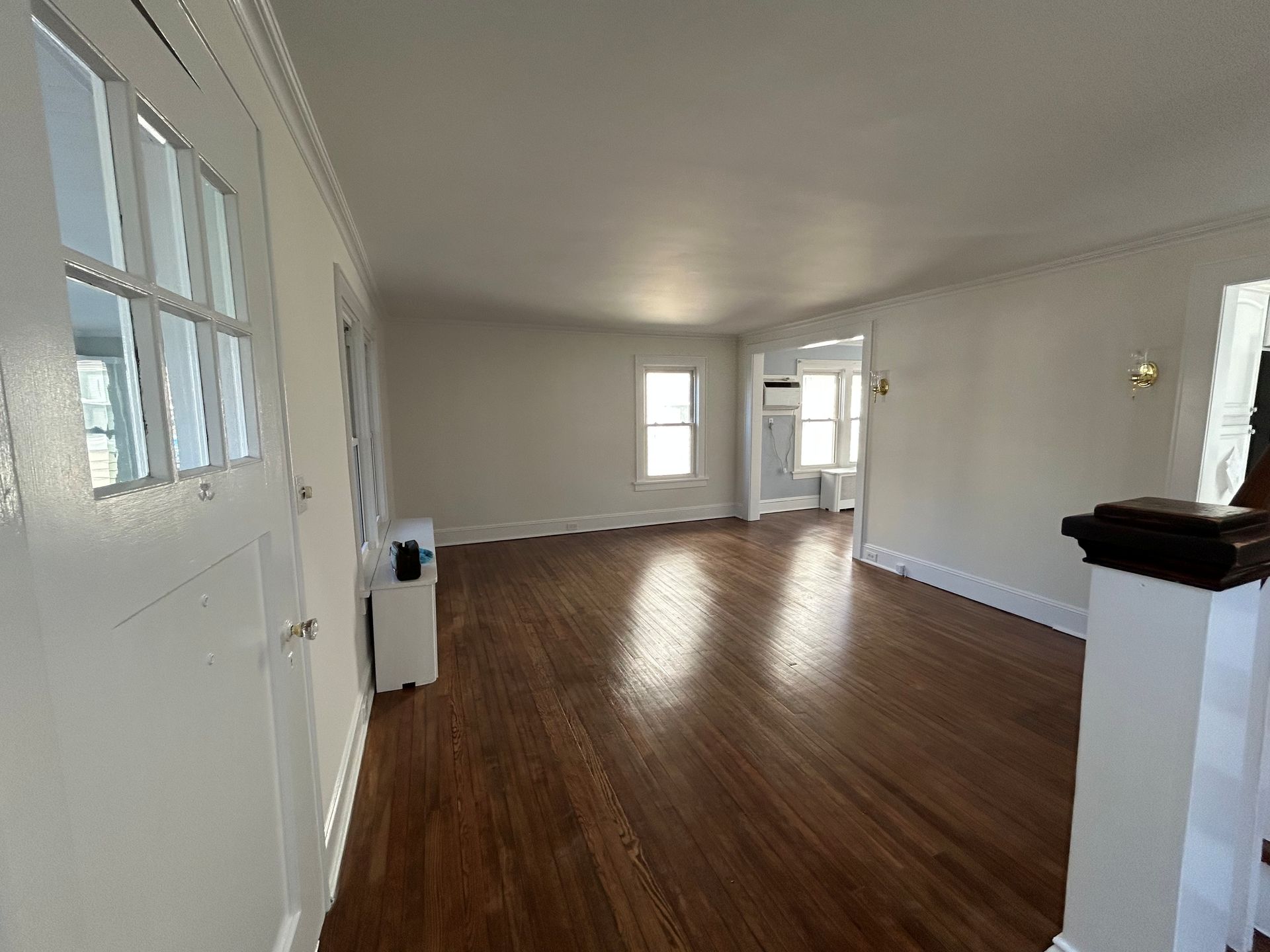Empty living room with wood floors, white walls, and large windows letting in daylight
