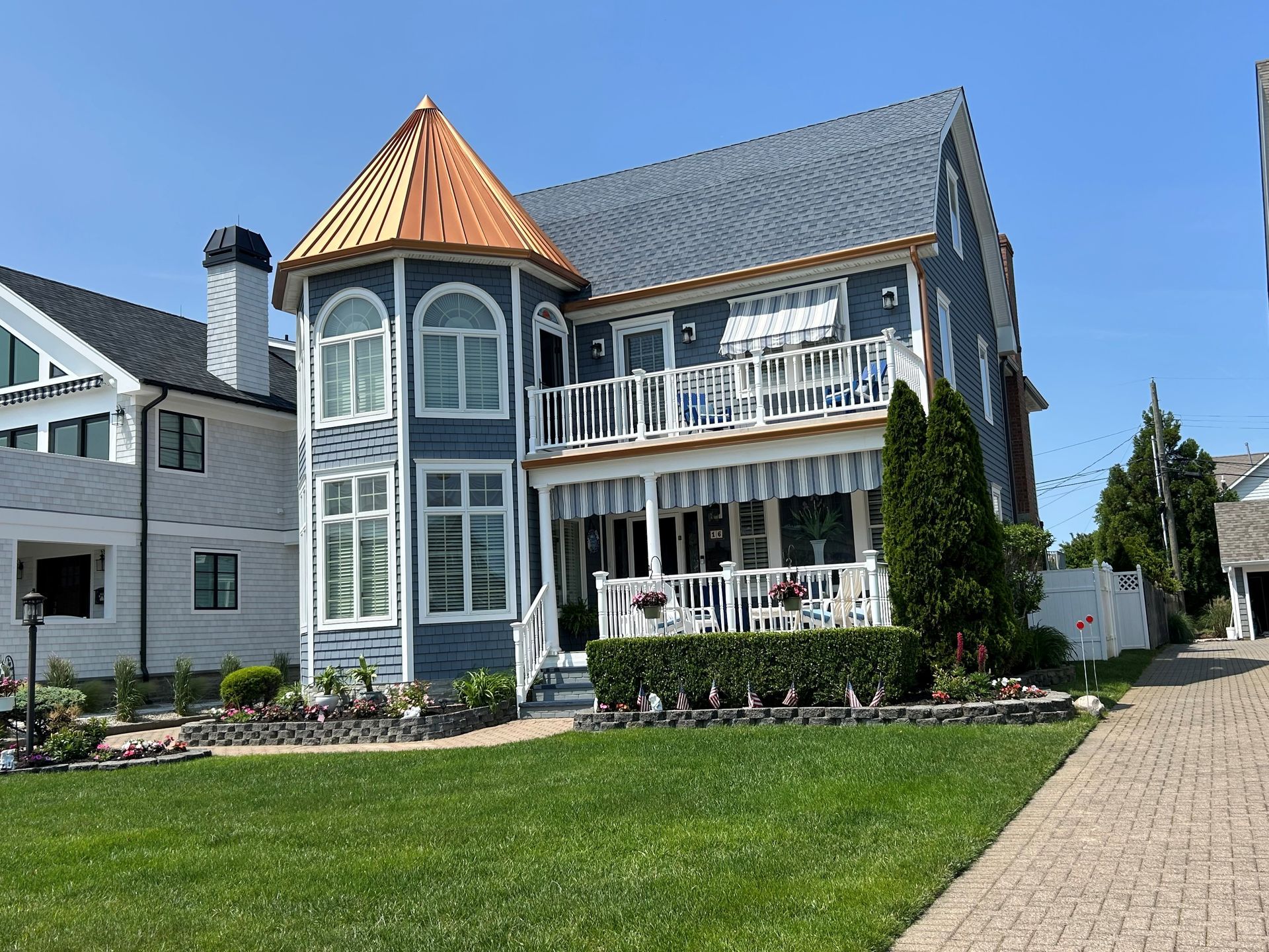 Victorian-style house with blue siding, orange turret roof, white balconies, and a green lawn by a sidewalk