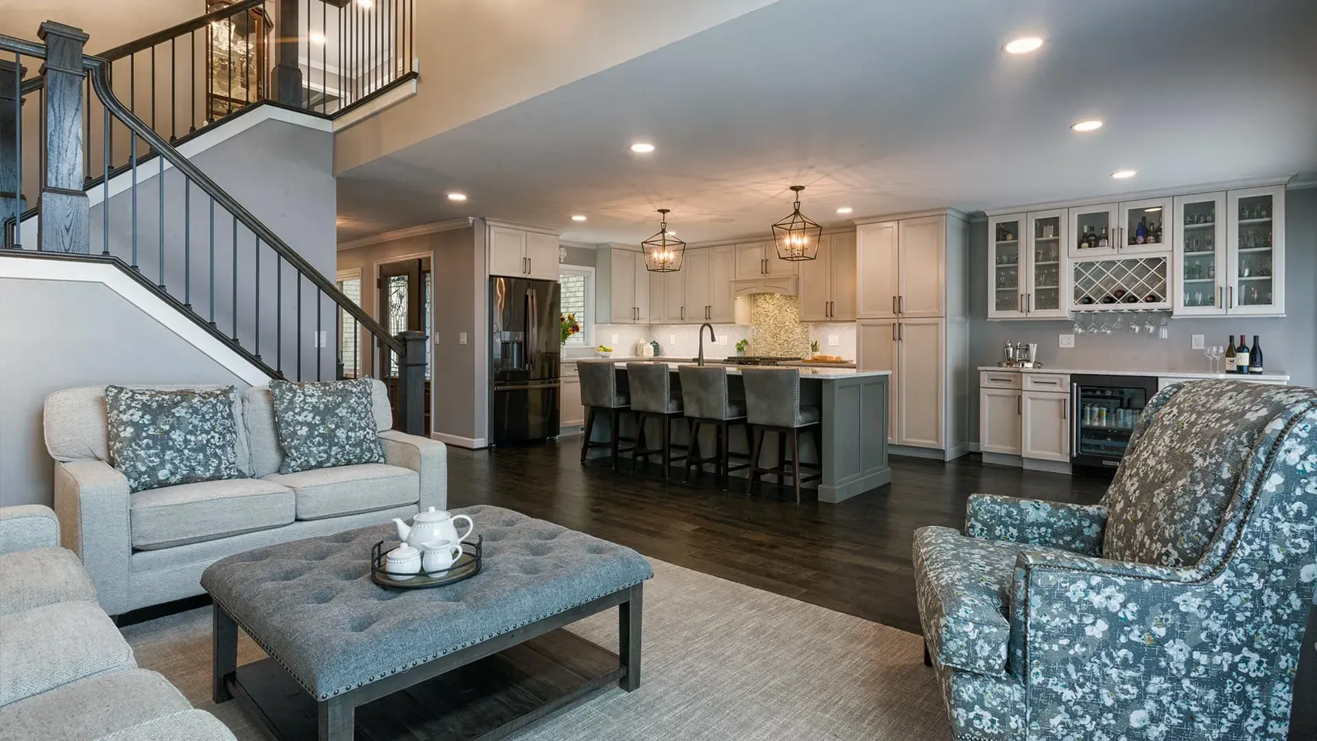 Open-plan living room with staircase, kitchen island, and gray-blue patterned furniture
