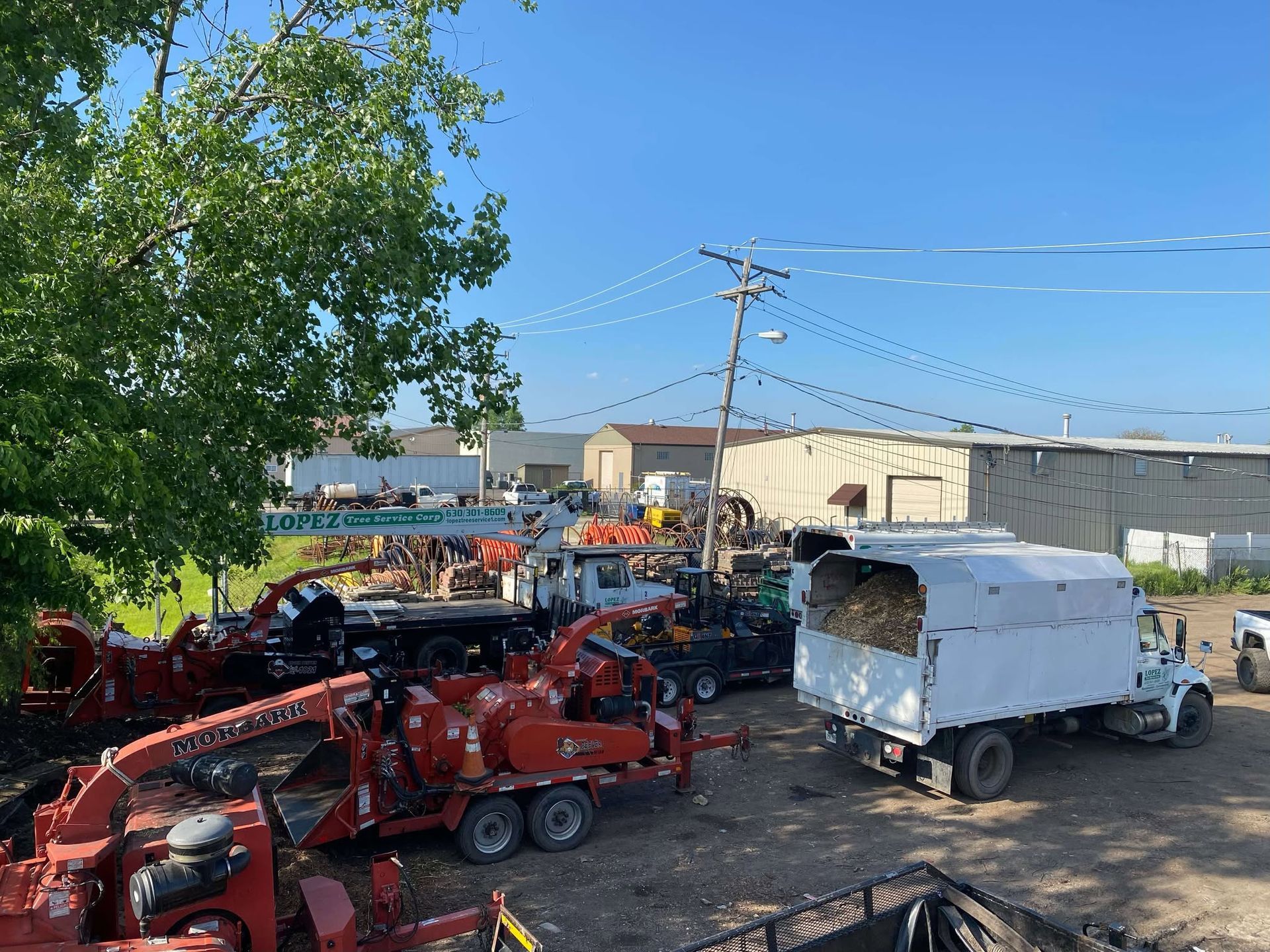 A yard filled with various wood chippers, a truck with wood chips, and industrial buildings under a blue sky.