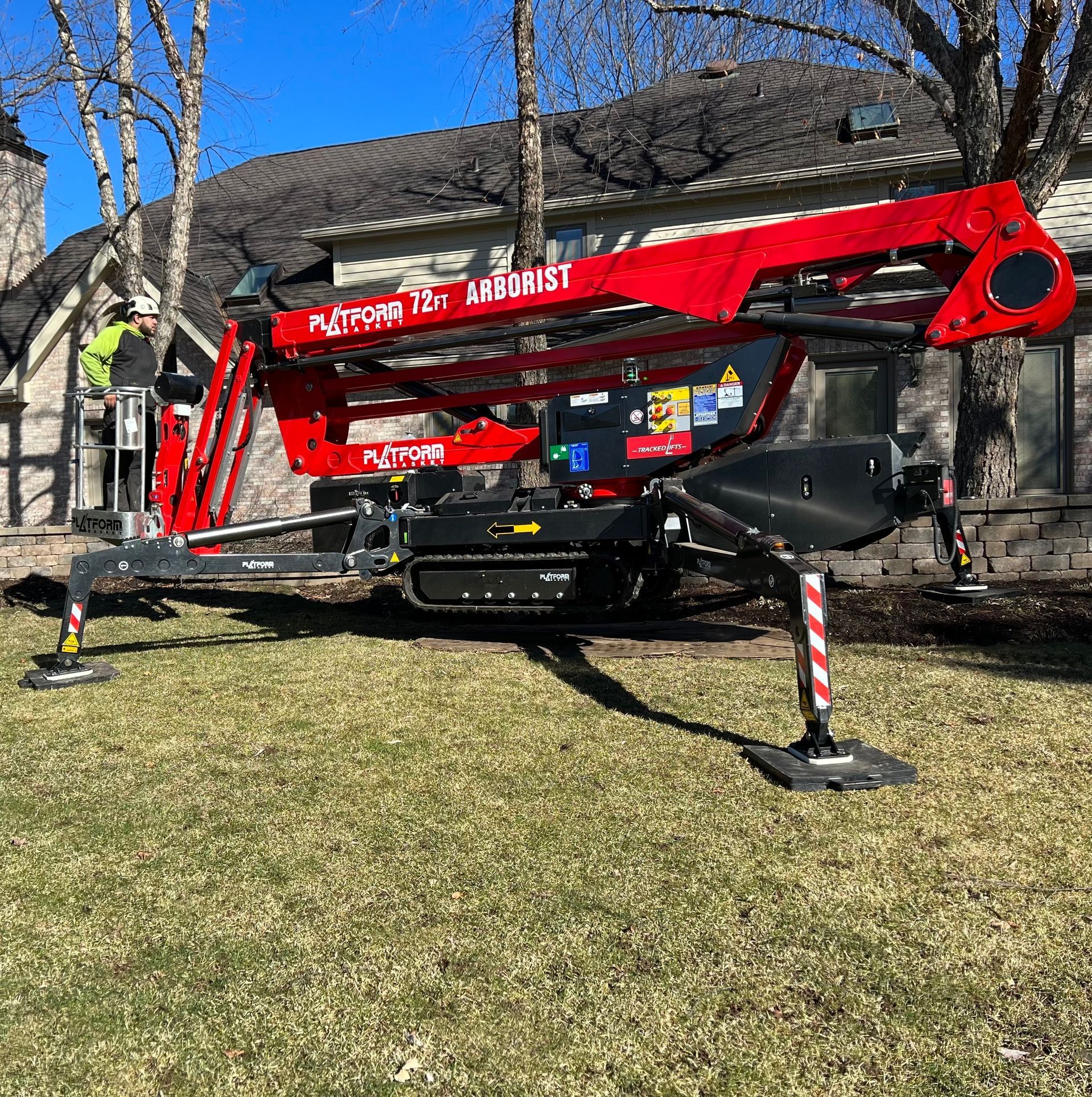 Red Platform 121 Arborist lift on green grass, next to a house; person operating the lift.