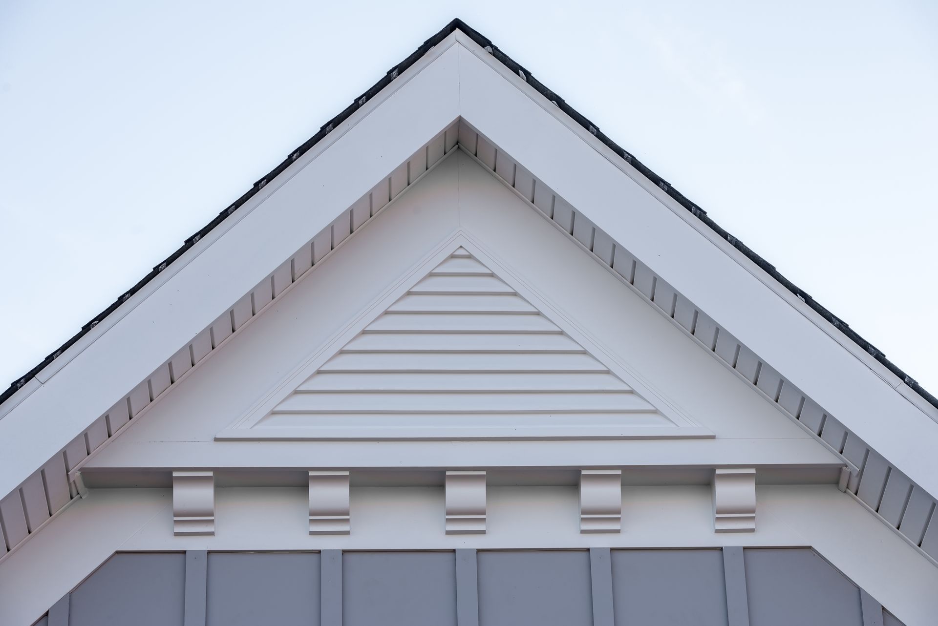 White house gable with gray trim and decorative vent details under the roof peak.