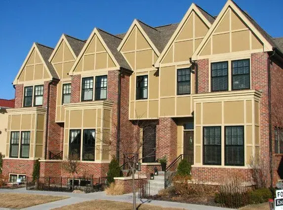Row of tan and red brick townhouses with peaked roofs and large windows in a suburban neighborhood.